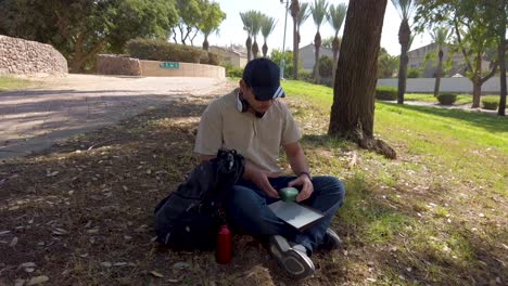 front view of a young man with glasses sitting on the grass of a park.