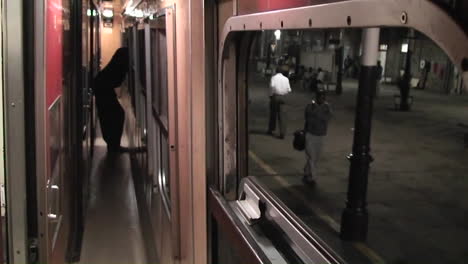 a person stands looking out the window as the train leaves the station and a man walks along on the platform