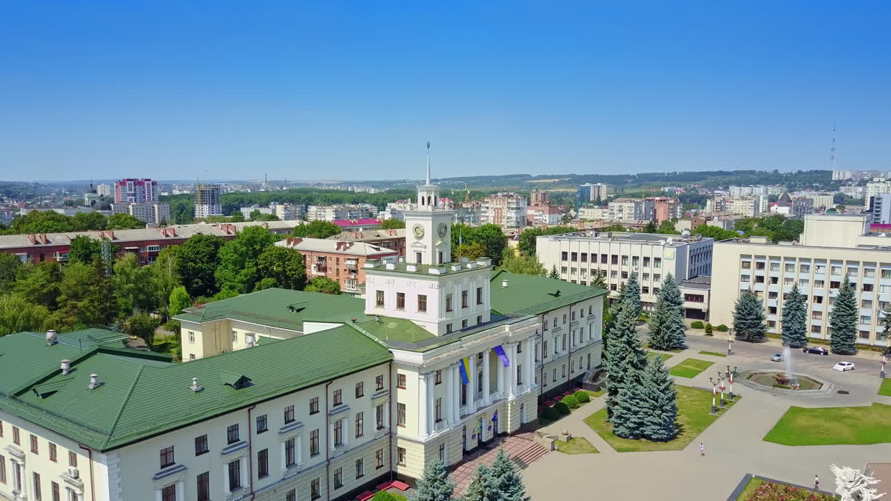 Rising above the beautiful Ukrainian city on sunny day. Wonderful governmental building with state flags and residential areas along with trees. Top view.