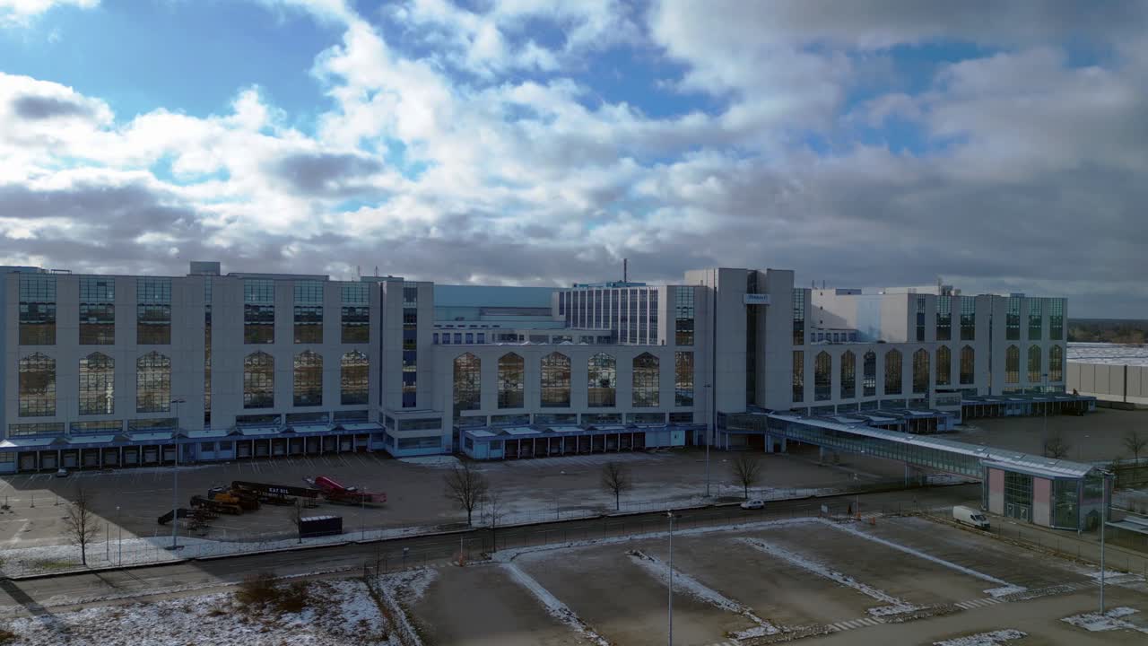 Large distribution center like an industrial castle with loading docks and parking lot under a cloudy sky in winter. Amazing aerial view flight static tripod hovering drone