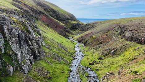 Río-Que-Fluye-A-Través-De-Un-Valle-Rocoso-Y-Verde-En-Islandia-Hacia-El-Océano,-Vista-Aérea