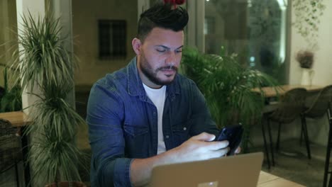 serious man using cell phone and laptop in coffee shop