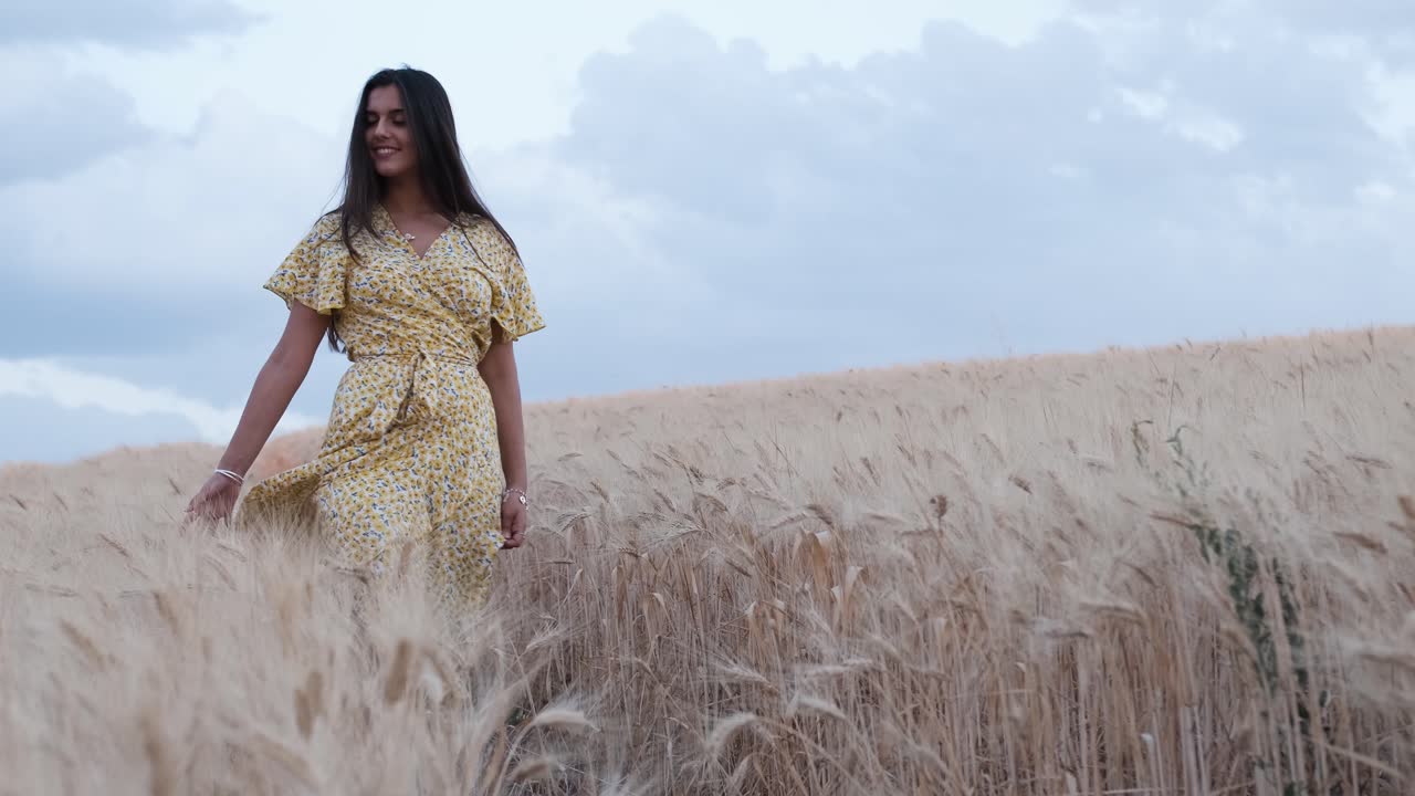 Front view of a woman touching wheat with her hand while walking through the field.