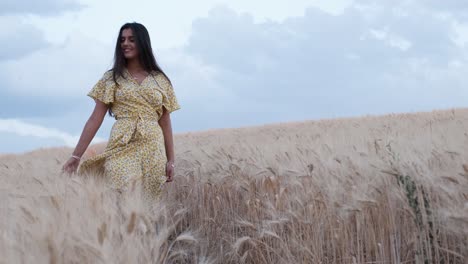 front view of a woman touching wheat with her hand while walking through the field.