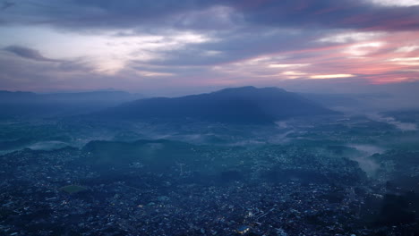 wide aerial footage in the blue light of the sunrise of the city of san juan ostuncalco and the mountains behind it in the haze