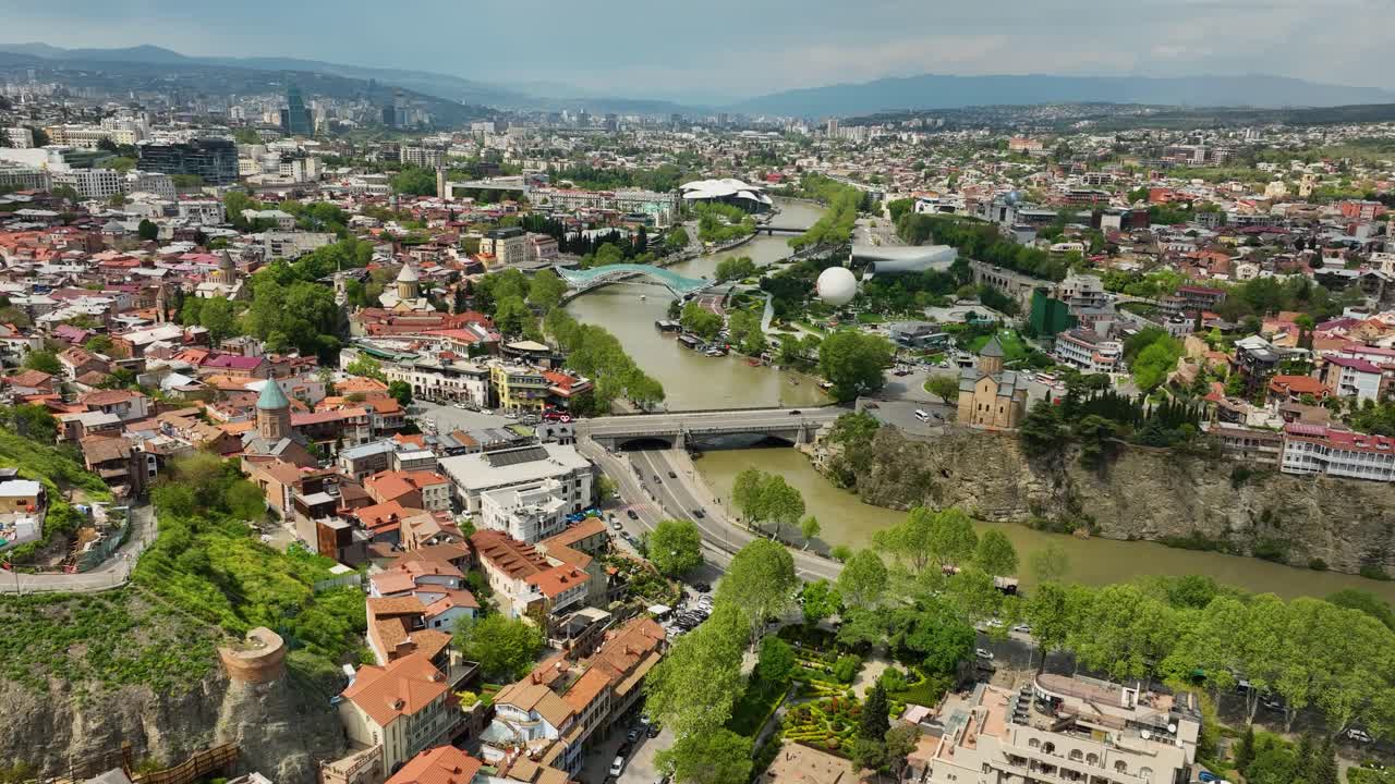 Ohromující panoramatický letecký pohled na město Tbilisi s řekou Kura vinoucí se městskou krajinou a střechami starého města pod ním