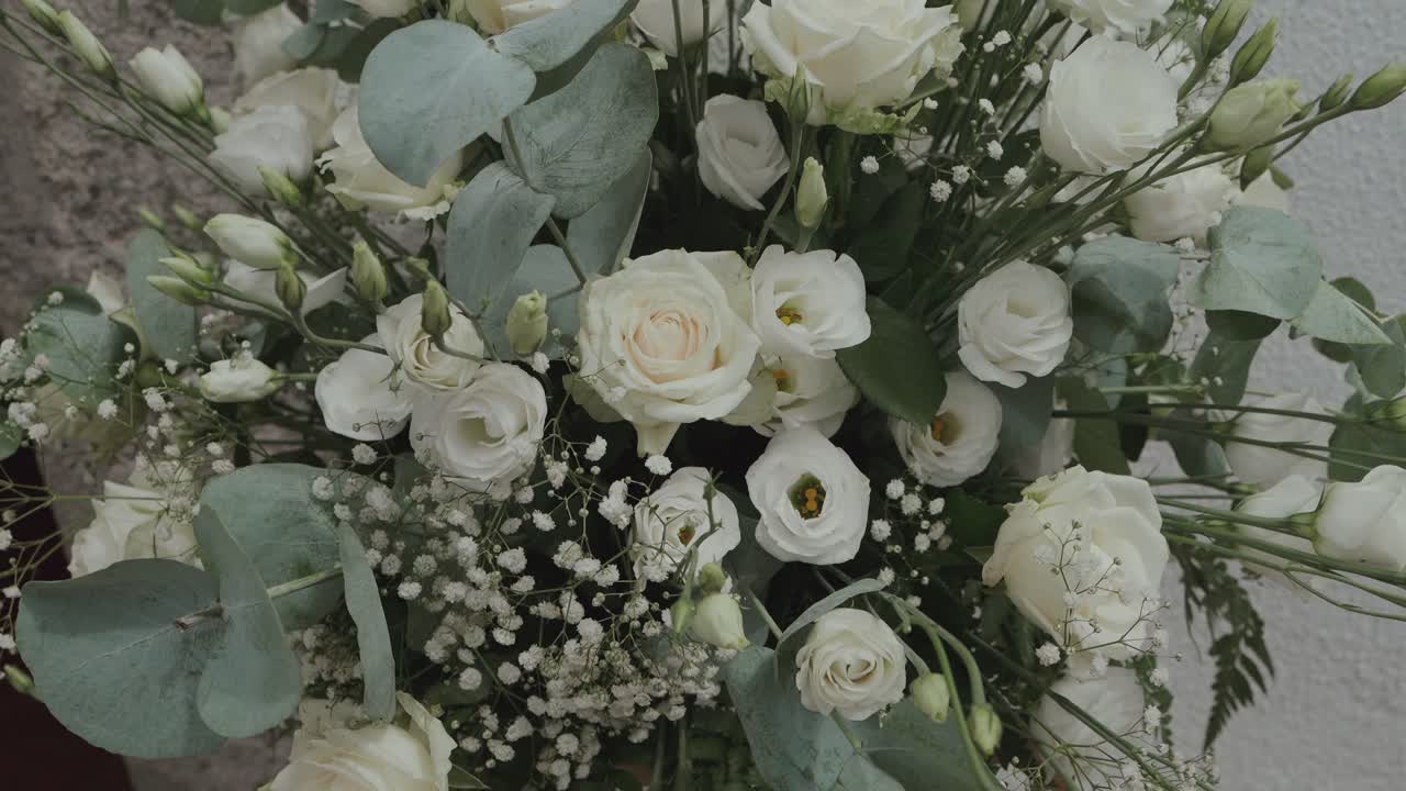 장미와 녹색 식물이 섬세하게 장식된 우아한 흰색 웨딩 플로럴 장식 클로즈업