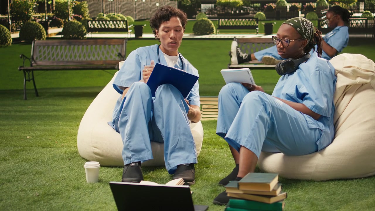 Diverse medical school peers in blue scrubs study on campus lawn