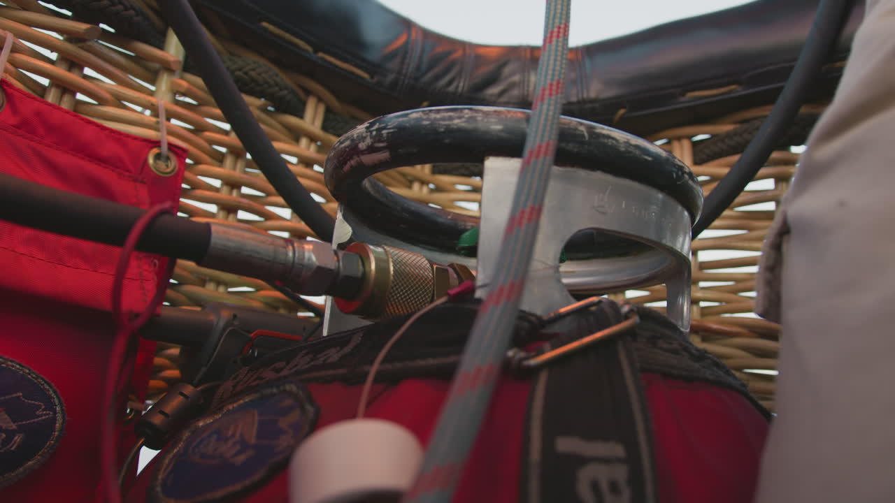 close up of metal ring, hose connector, and red bag inside hot air balloon basket showing technical details of propane burner attachment with wicker background