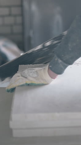 skilled repairman in special gloves holds big saw and starts cutting white gypsum plasterboard put on table close view