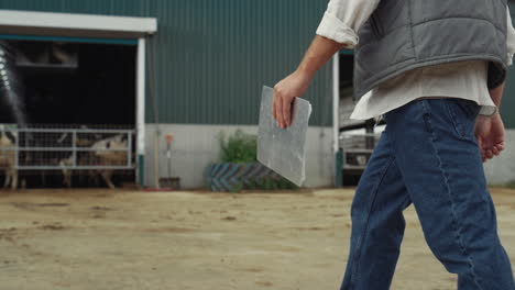 Farm-worker-walking-livestock-facility.-Hand-holding-clipboard-legs-closeup.