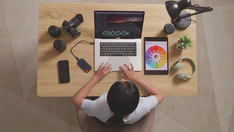 top view of a woman editor looking at the color schemes on a tablet while sitting in the workspace using a laptop next to the camera editing the video at home