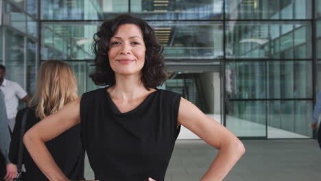 Portrait-Of-Mature-Businesswoman-Standing-In-Lobby-Of-Busy-Modern-Office