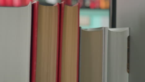 close up side view of young man in casual shirt and backward cap browsing colorful bookshelf in modern library, scanning book titles with focused expression against turquoise wall background