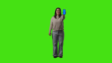 fotografía completa de una mujer con gafas sosteniendo un teléfono móvil de pantalla azul en la cámara contra el fondo de la pantalla verde 1