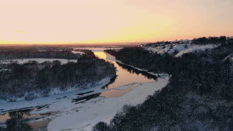 sunset over frozen river and evergreen forest. country highway passing across water at winter season.