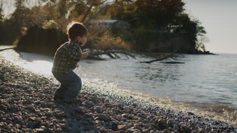 asian kid having fun on the shore of the lake - throws stones into the water.