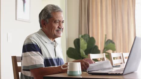 biracial senior man doing paperwork and using laptop at home, slow motion