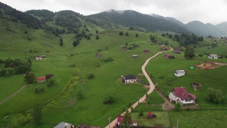 Sirnea-village-in-romania-with-scattered-houses-and-lush-green-hills-on-overcast-day,-aerial-view