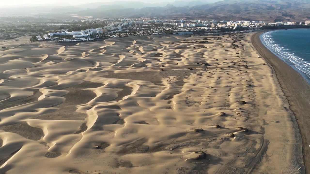 Maspalomas dunes border a curving Atlantic beach and coastal resort on Gran Canaria, aerial