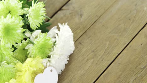 bunch of yellow flowers with heart shape tag on wooden plank