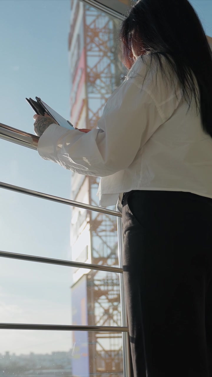 Young woman with long dark hair wearing white blouse. Woman interacts subtly while positioned by metal railings. Camera captures slight downward angle shifts focusing