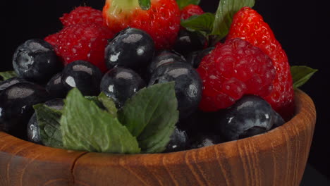 Rotating-delicious-forest-berries-in-a-wooden-bowl,-wet-bright-fruits,-strawberries,-blueberries,-raspberries,-4K-macro-shot