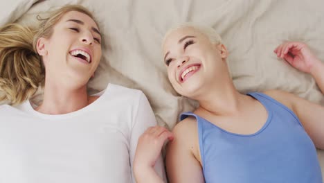 happy diverse female couple embracing and lying together in bed