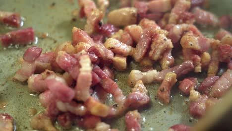 fat and unhealthy bacon frying in pan, wooden spoon stirring, extreme close-up