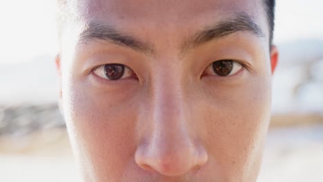 Portrait-close-up-of-happy-asian-man-looking-at-camera-at-promenade-by-the-sea,-slow-motion