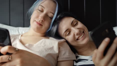 front view video of women lying with phones in bed.