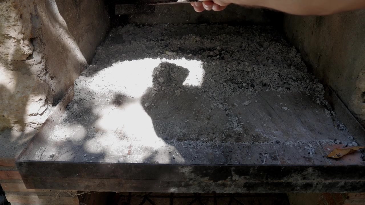 El, rustik dış mekan barbekü ızgarasının yüzeyinden külü temizlemek için metal bir alet kullanıyor