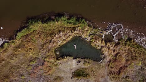 Frau-Schwimmt-In-Einem-Thermalbecken-In-Der-Nähe-Eines-Flusses,-Tritt-Auf-Wasser-Und-Genießt-Die-Wunderschöne-Landschaft