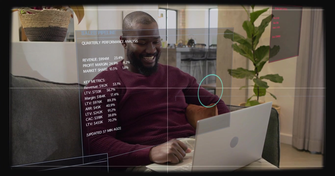 Man gesturing and tapping laptop on sofa, HUD panels appearing while reviewing business metrics