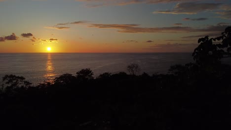 An-aerial-drone-discovers-the-mesmerizing-Uvita-Beach-sunset-in-Costa-Rica:-an-enchanting-orange-sun-casting-its-glow-upon-the-sea,-showcasing-vibrant-natural-beauty