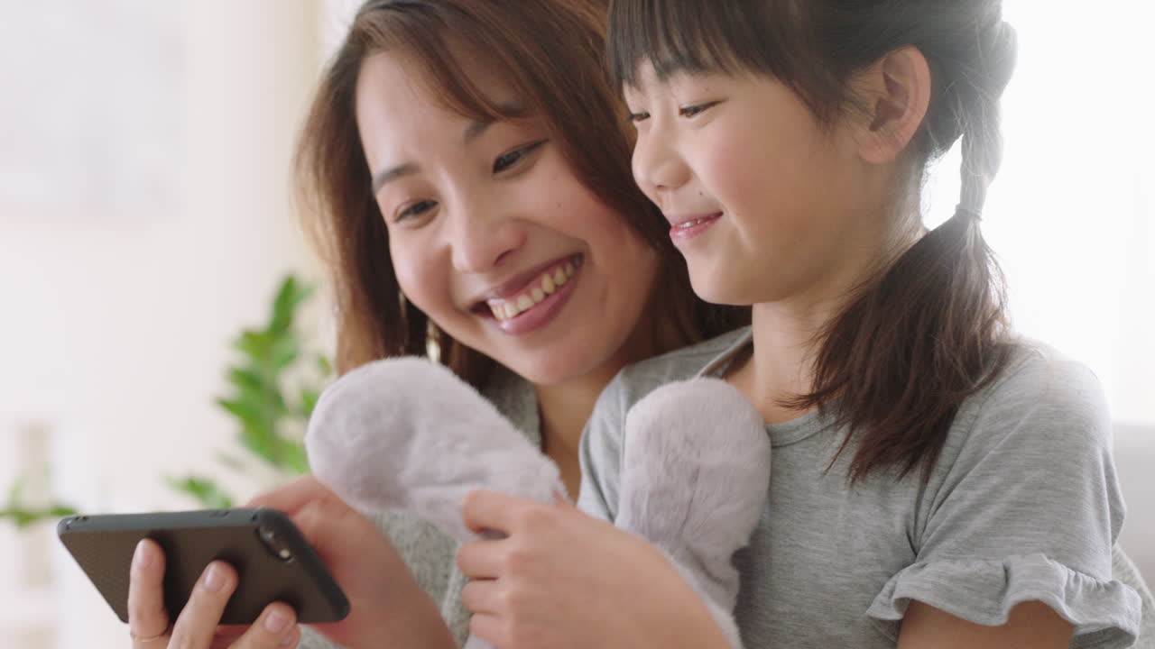 アジアの母親と子供がスマートフォンを使ってビデオチャットをしています 母親と小さな女の子が手を振って 娘と週末の休暇を共有しています 携帯電話でチャットを楽しんでいます 4k映像
