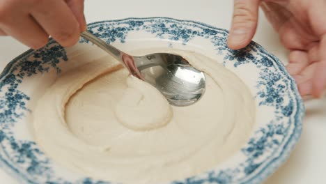 la persona prepara un plato de hummus para servir, un delicioso refrigerio vegetariano