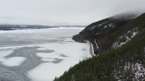 a partially frozen lake in between mountains with a road