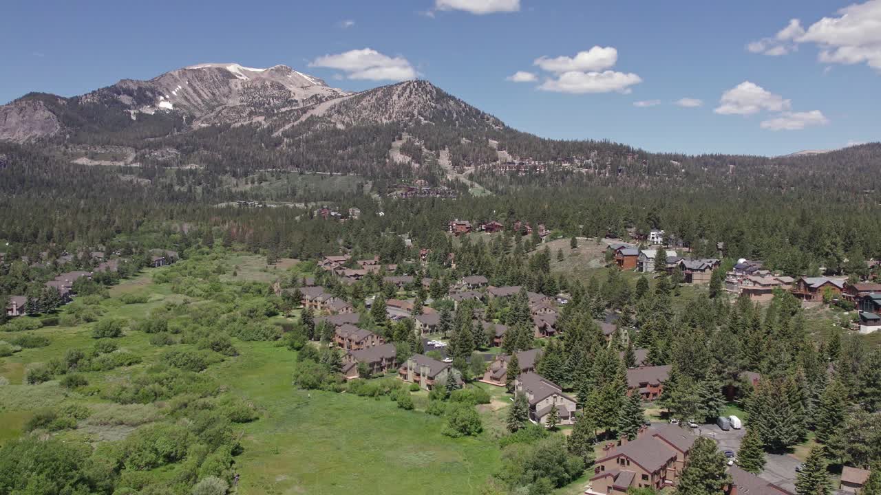Filmato drone 4k con lenta rotazione della telecamera che riprende la splendida Mammoth Mountain in estate, con vista su un prato verde lussureggiante e baite.