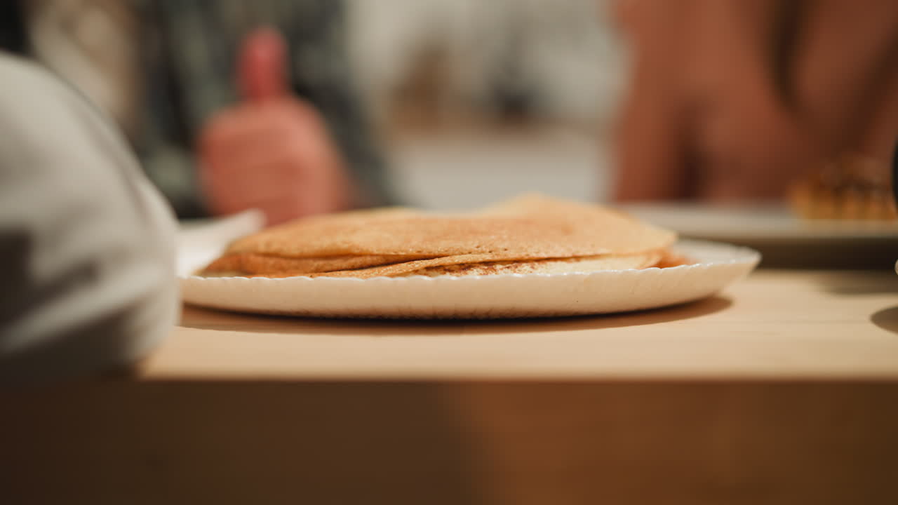 을 입은 여성 손은 테이블에 달한 팬케이크를 놓습니다.