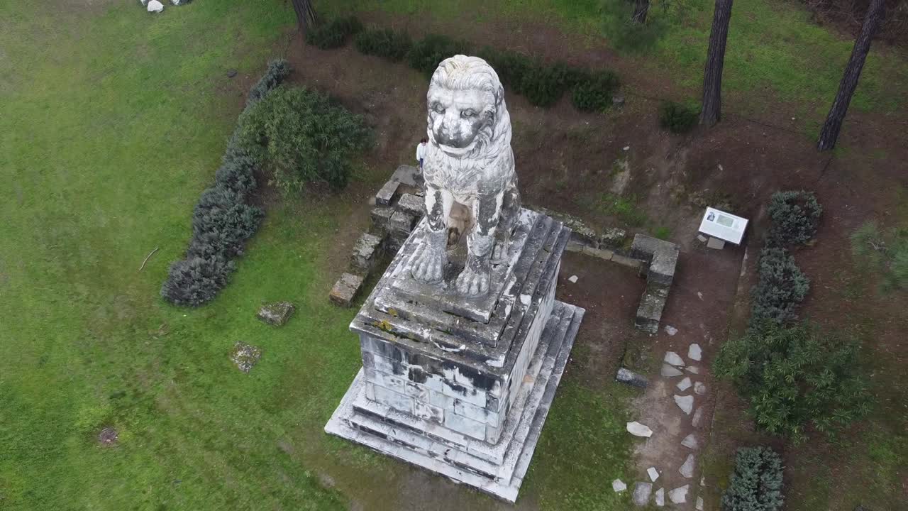 Una toma aérea suave con retroceso que revela el León de Anfípolis del siglo IV a.C. desde una perspectiva cenital. Un majestuoso símbolo de mármol del poder macedonio y la gloria militar en el norte de Grecia.