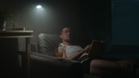 a sad man reads a book at night in his underwear