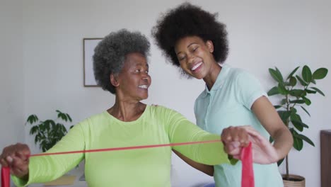 Happy-african-american-female-physiotherapist-helping-senior-female-patient-exercise-at-home