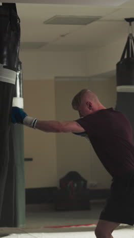 el hombre fuerte patea la bolsa de boxeo con las rodillas en el gimnasio. el kickboxer hábil hace ejercicios con equipos en el club deportivo en cámara lenta. el hombre fuerte entrena en combate.