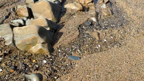 Close-up-of-a-small-water-stream-along-the-beach-that-flows-to-the-sea-between-some-rocks