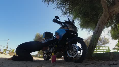 joven revisa el nivel de aceite de la motocicleta a la sombra del árbol de la playa