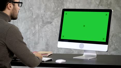 elegant businessman analyzing data in office on his computer. back view to the monitor. green screen mock-up display