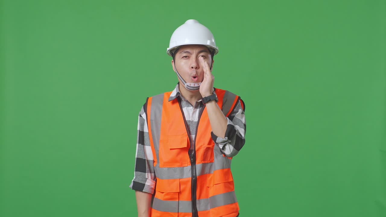 Asian Male Engineer With Safety Helmet Yelling With Hand Over Mouth While Standing In The Green Screen Background Studio
