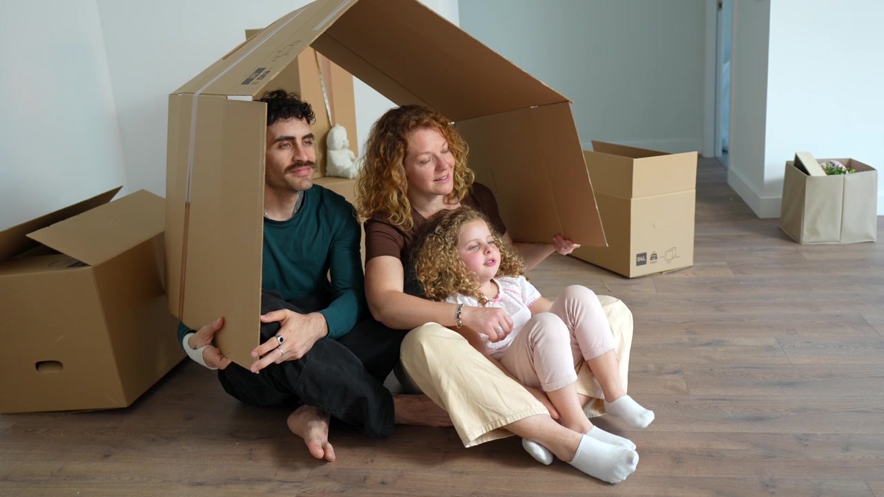 Happy Family Sitting Inside a Cardboard House in Their New Home