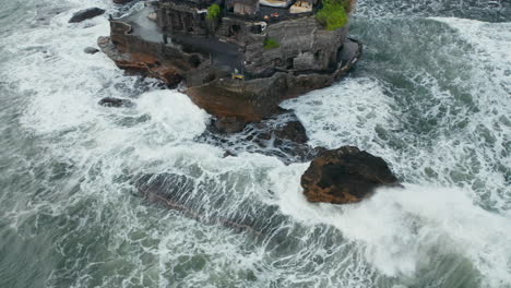 Vista-Aérea-De-Rocas-Peligrosas-Y-Fuertes-Olas-Que-Se-Estrellan-Contra-El-Acantilado-De-La-Costa-Con-El-Templo-De-Tanah-Lot-En-Bali,-Indonesia